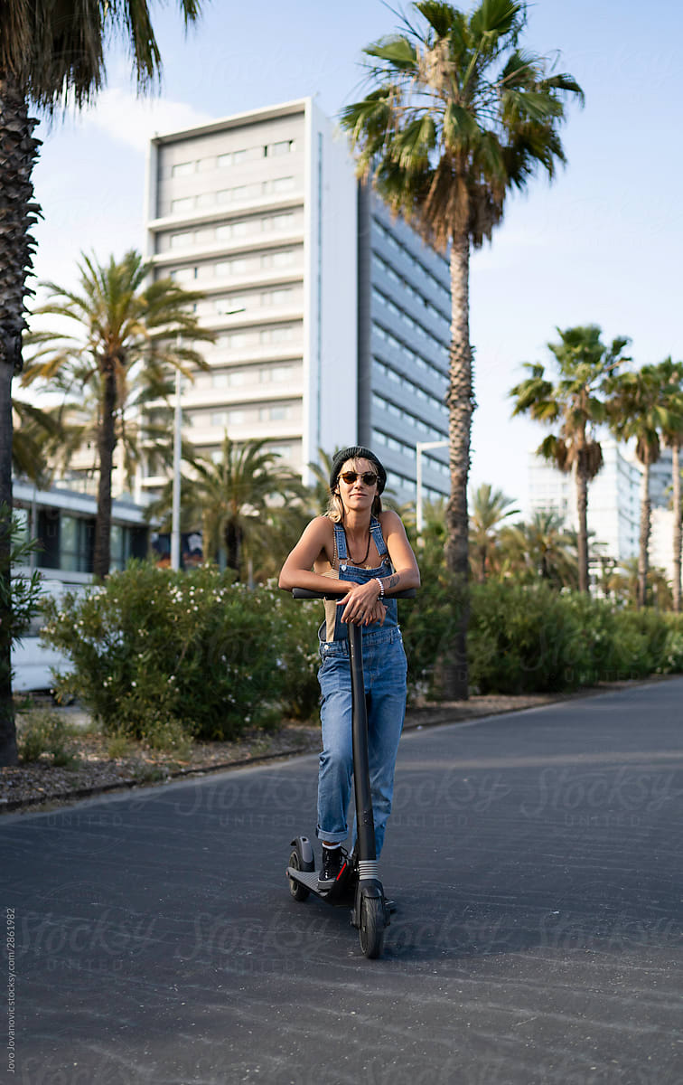 Young woman with sunglasses resting on electric scooter outside
