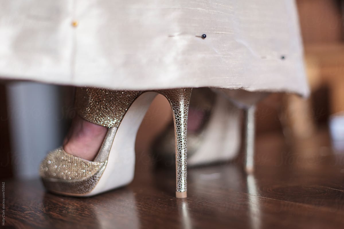 Women\'s feet in sexy, gold heels peek out from hemline