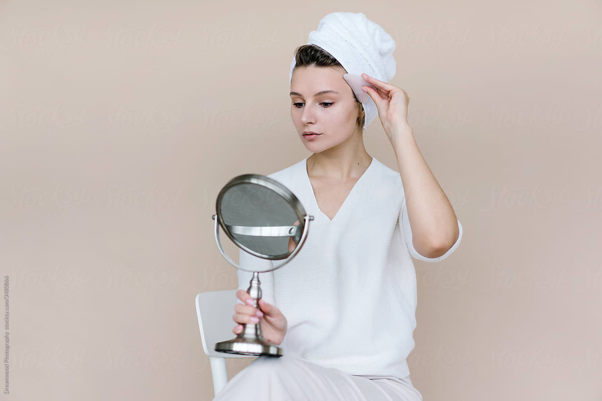 Woman with mirror doing facial Gua Sha massage at home