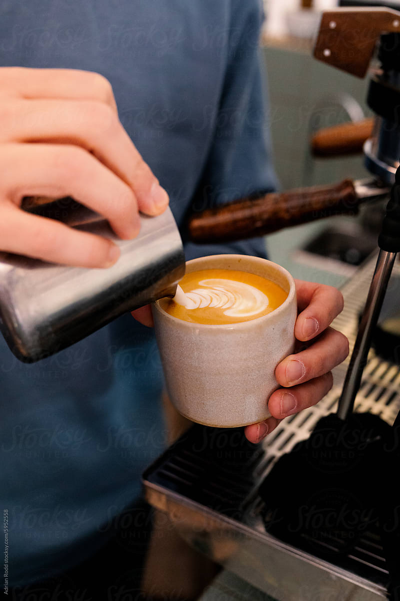 The hands of a professional barista making latte art flat white coffee