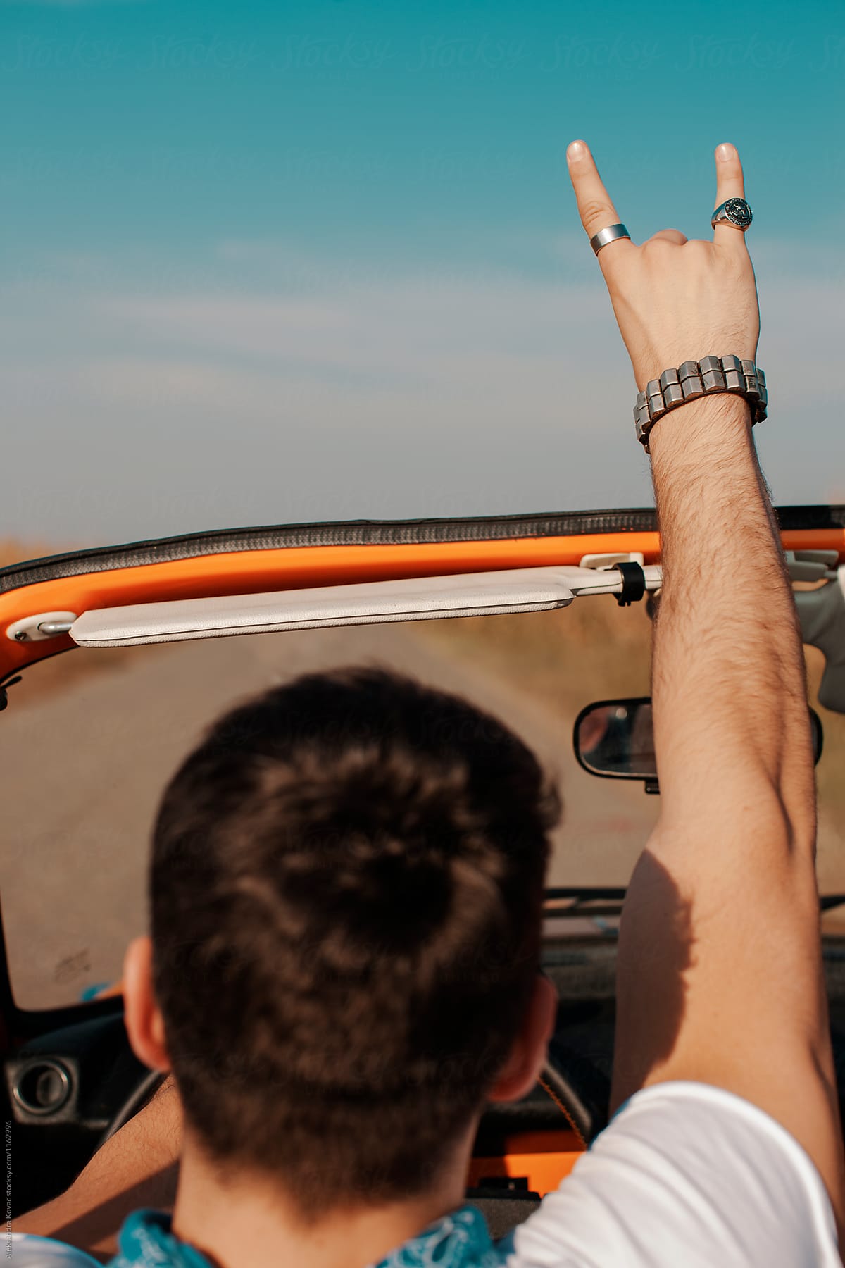 Man in convertible car shows a rock and roll hand sign