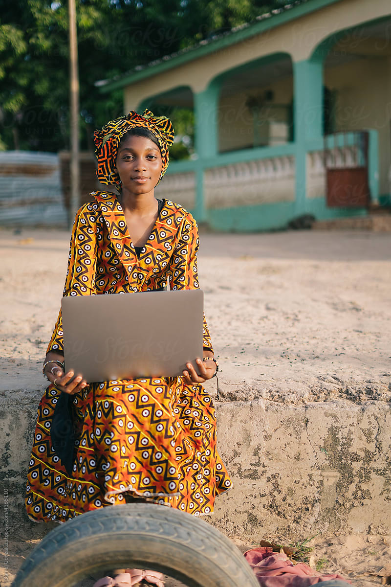 African lady with laptop sitting on village street