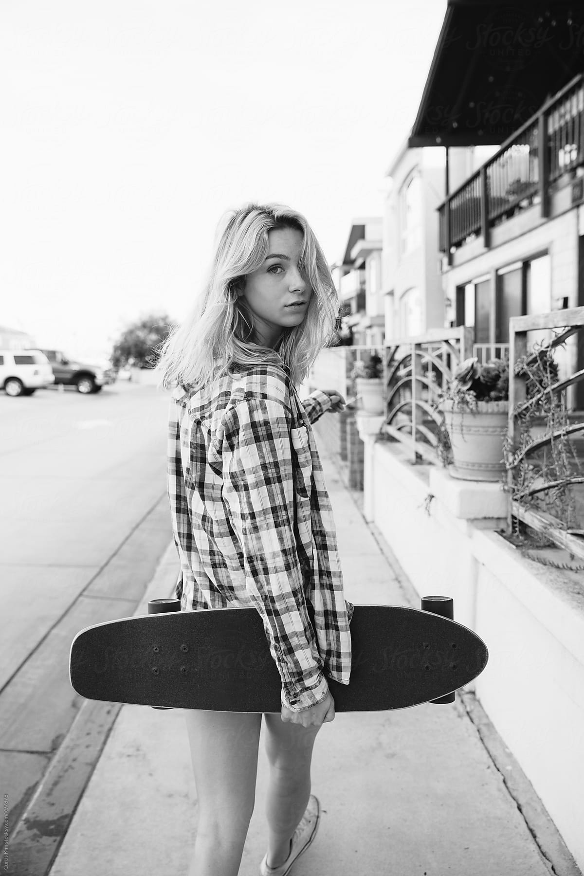 Blonde girl walking down sidewalk holding skateboard