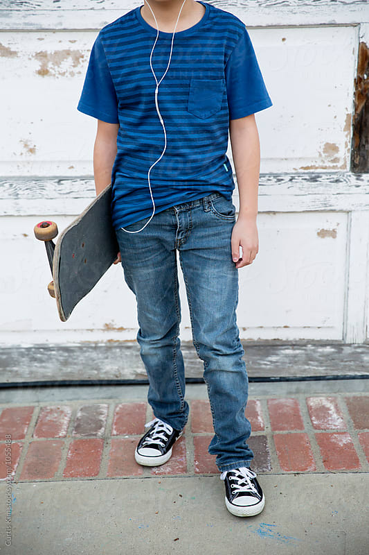 Young kid holding skateboard and listening to his earphones