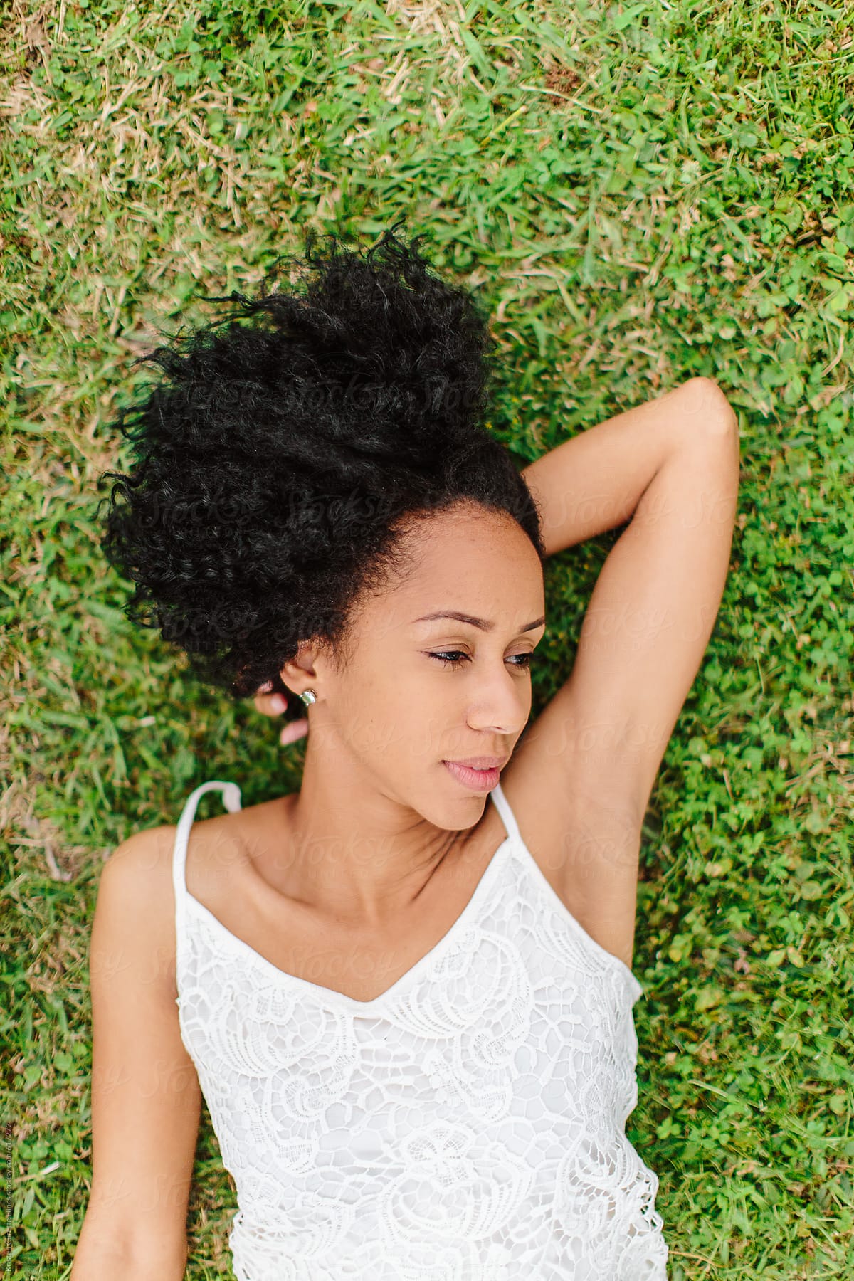 A Beautiful Woman With Curly Hair Laying Down In The Grass Daydreaming