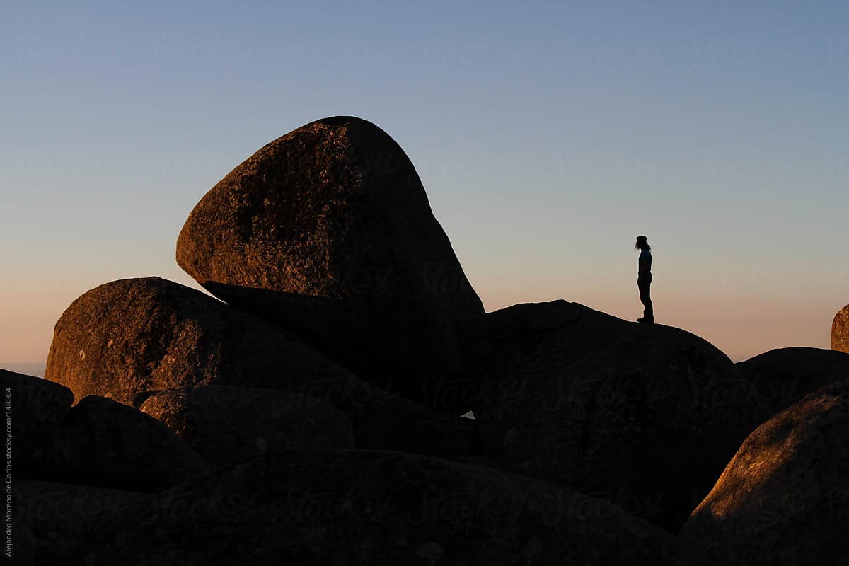 Man silhouette on top of a boulder at sunrise