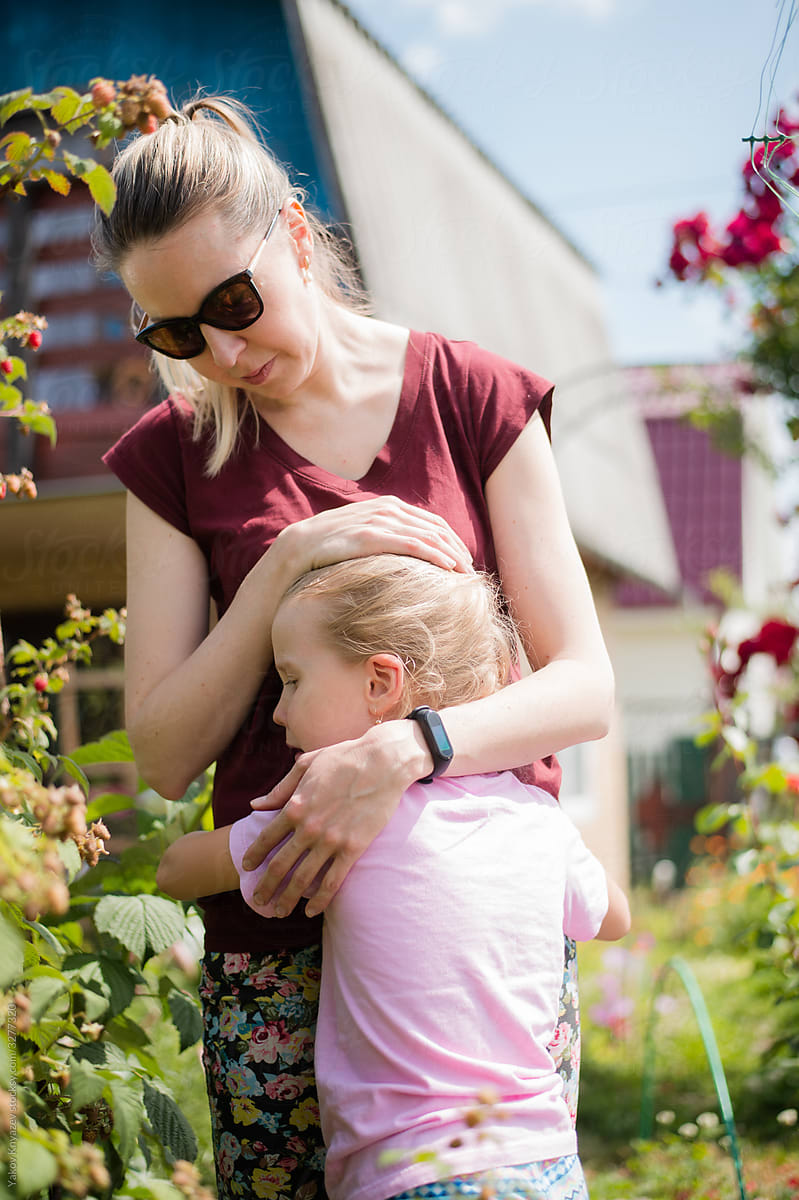 cute blonde girl cries hugging her mother in the garden
