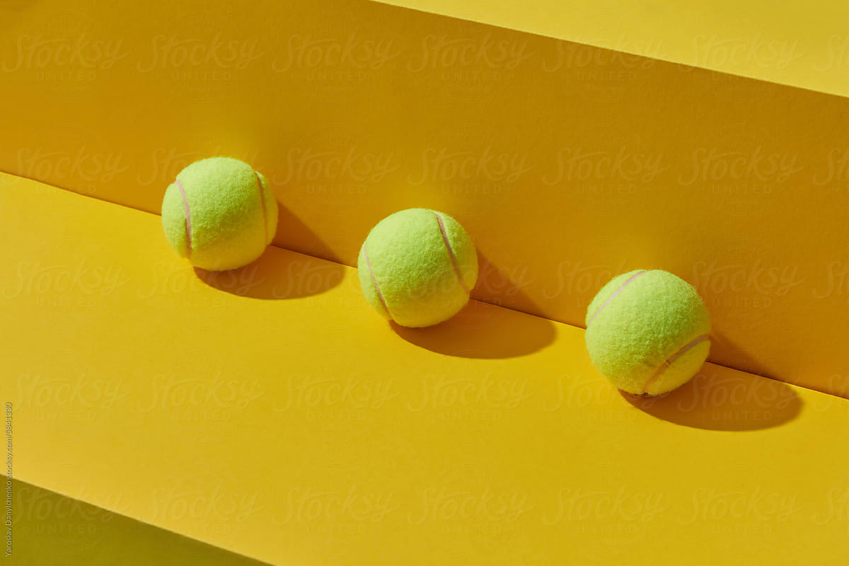Three tennis balls arranged in line near yellow wall in studio