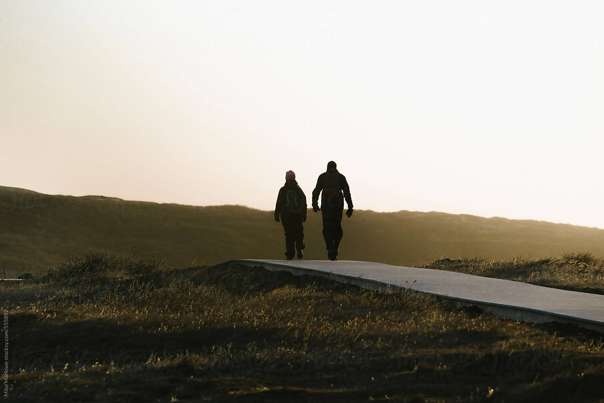 Silhouette Of Two People Walking Away In To The Distance At Sunset