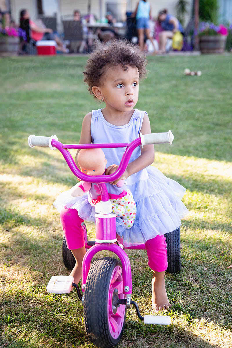 Curly haired toddler sitting on a pink tricycle