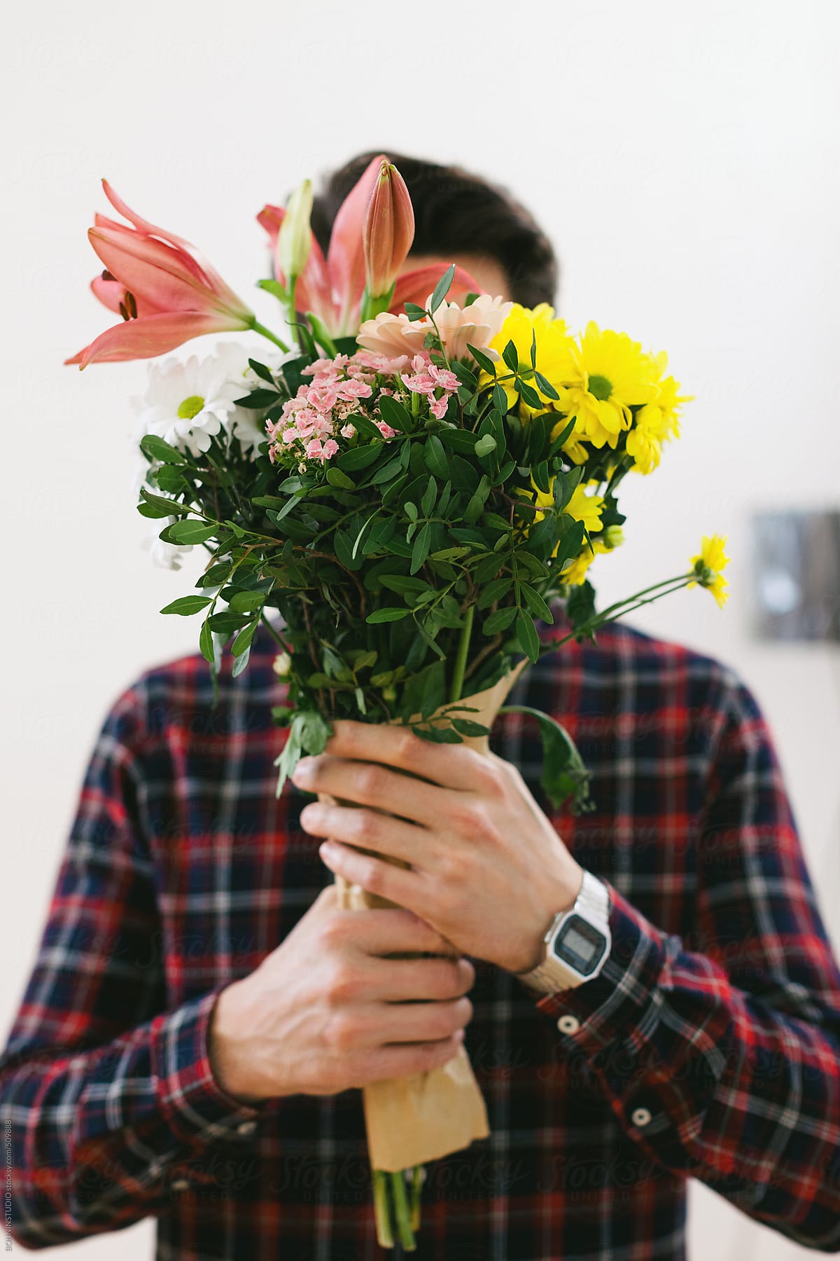 Young man covering his face with a bouquet of flowers.