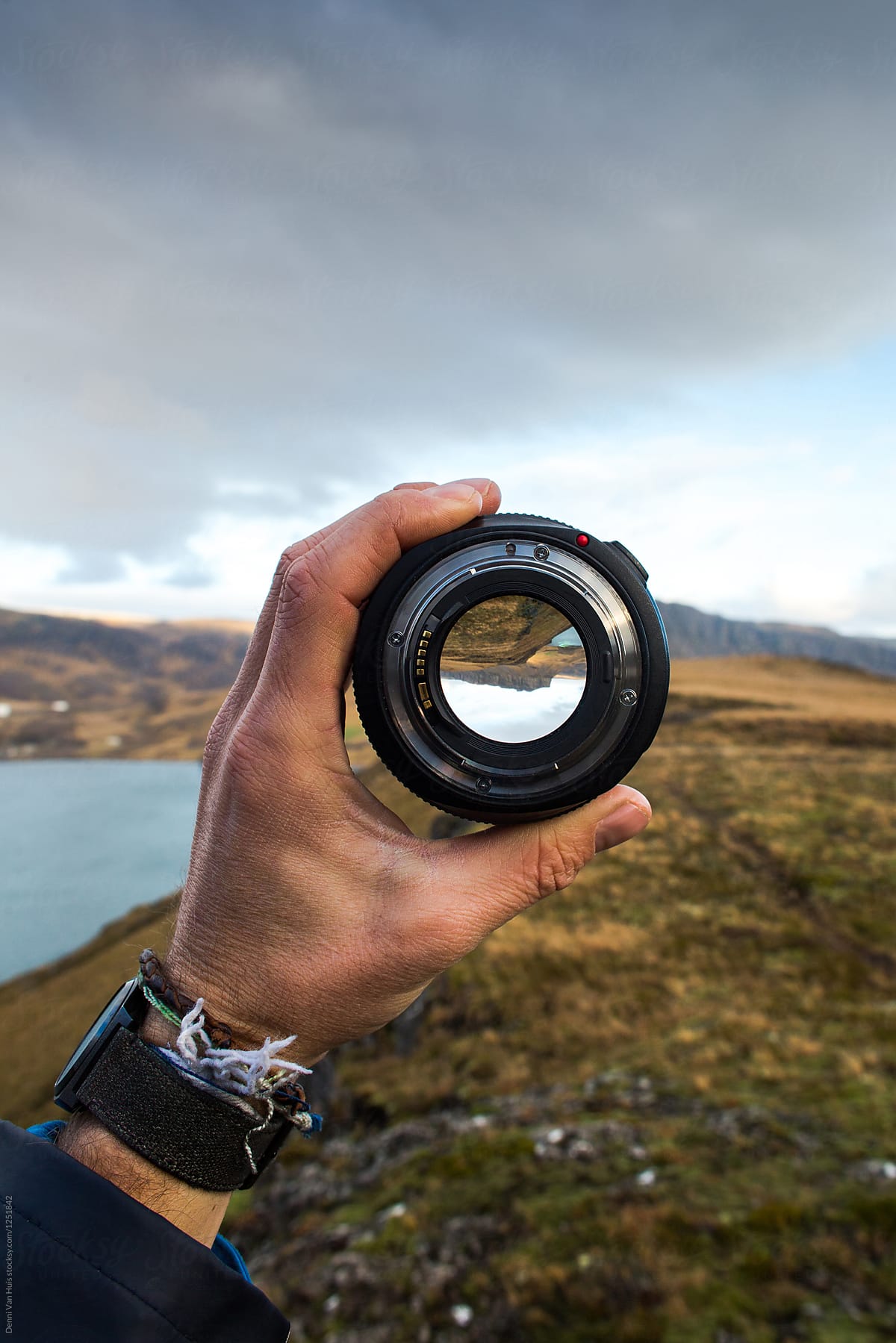Hand holding up a camera lens and looks through it surrounded by a beautiful landscape.