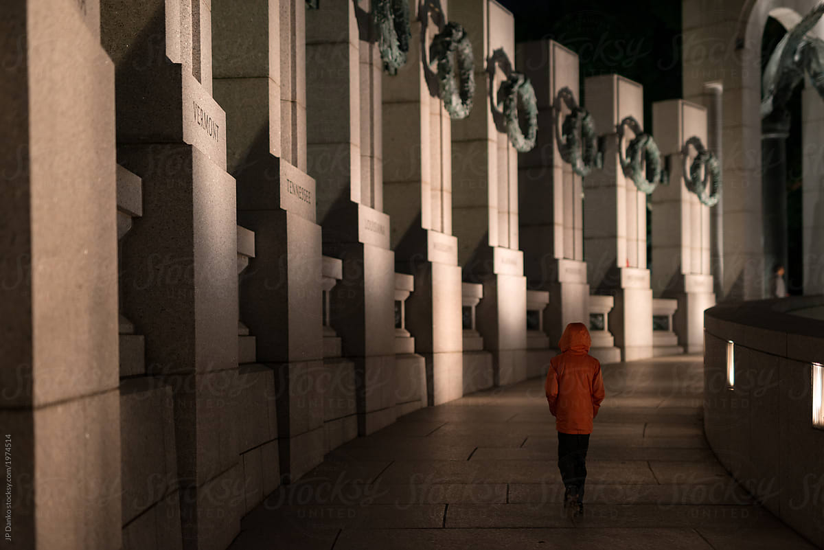 Boy alone at night walks quietly reflecting through World War II memorial