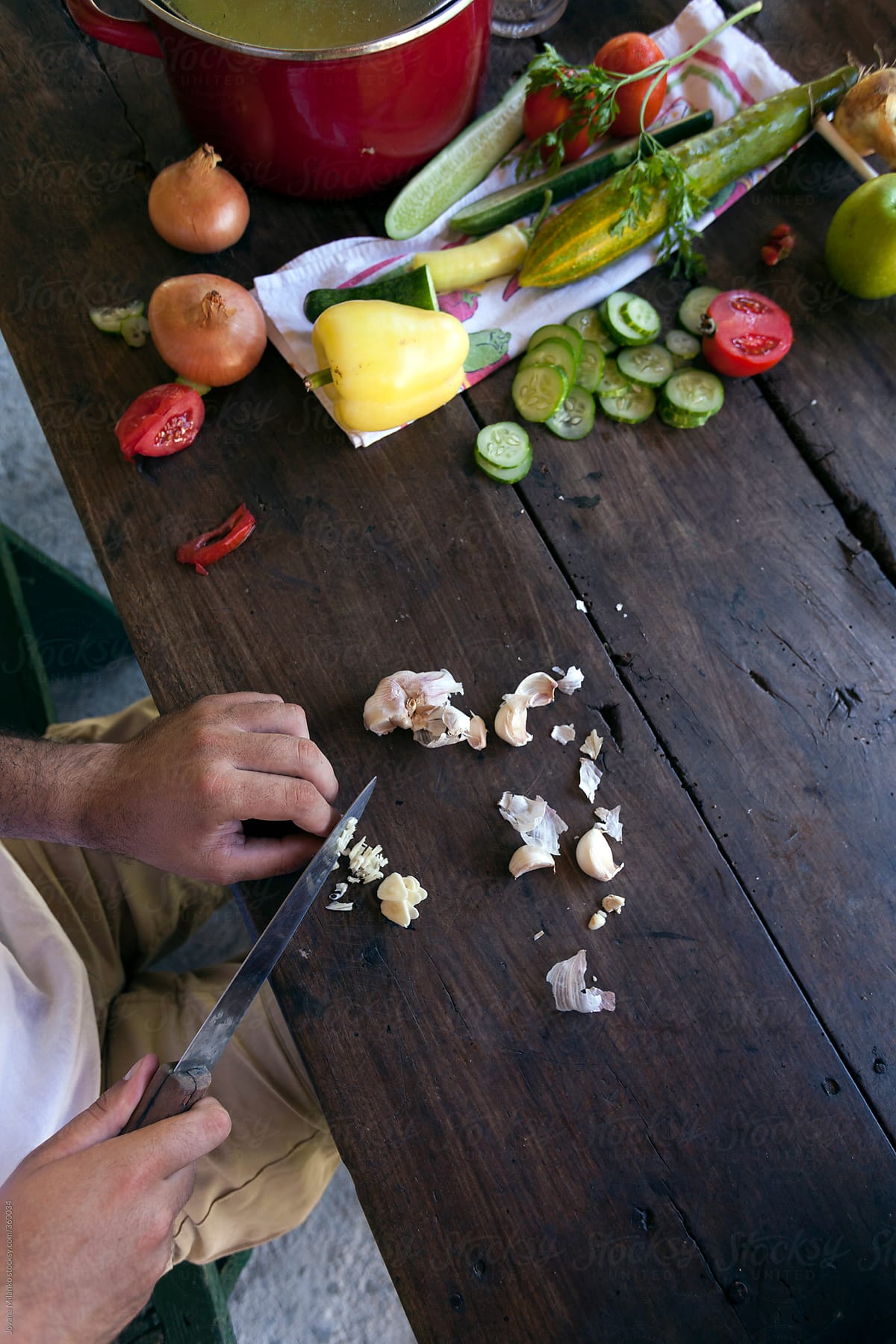 Man cutting garlic on the rustic brown table covered with vegetables