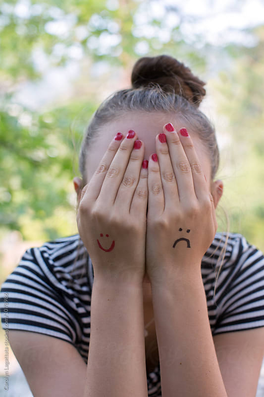 Teenage girl with a smiley and a frown drawn on her hands