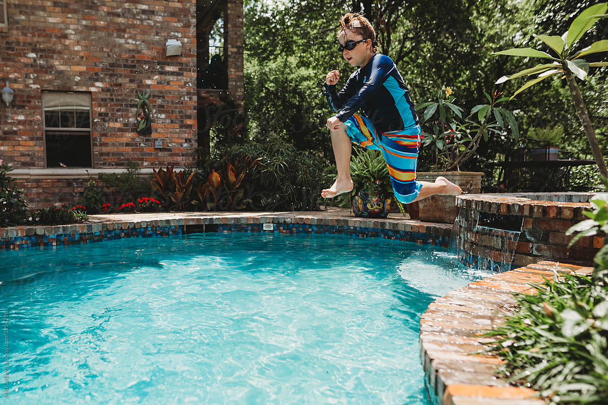 Boy jumping into backyard swimming pool