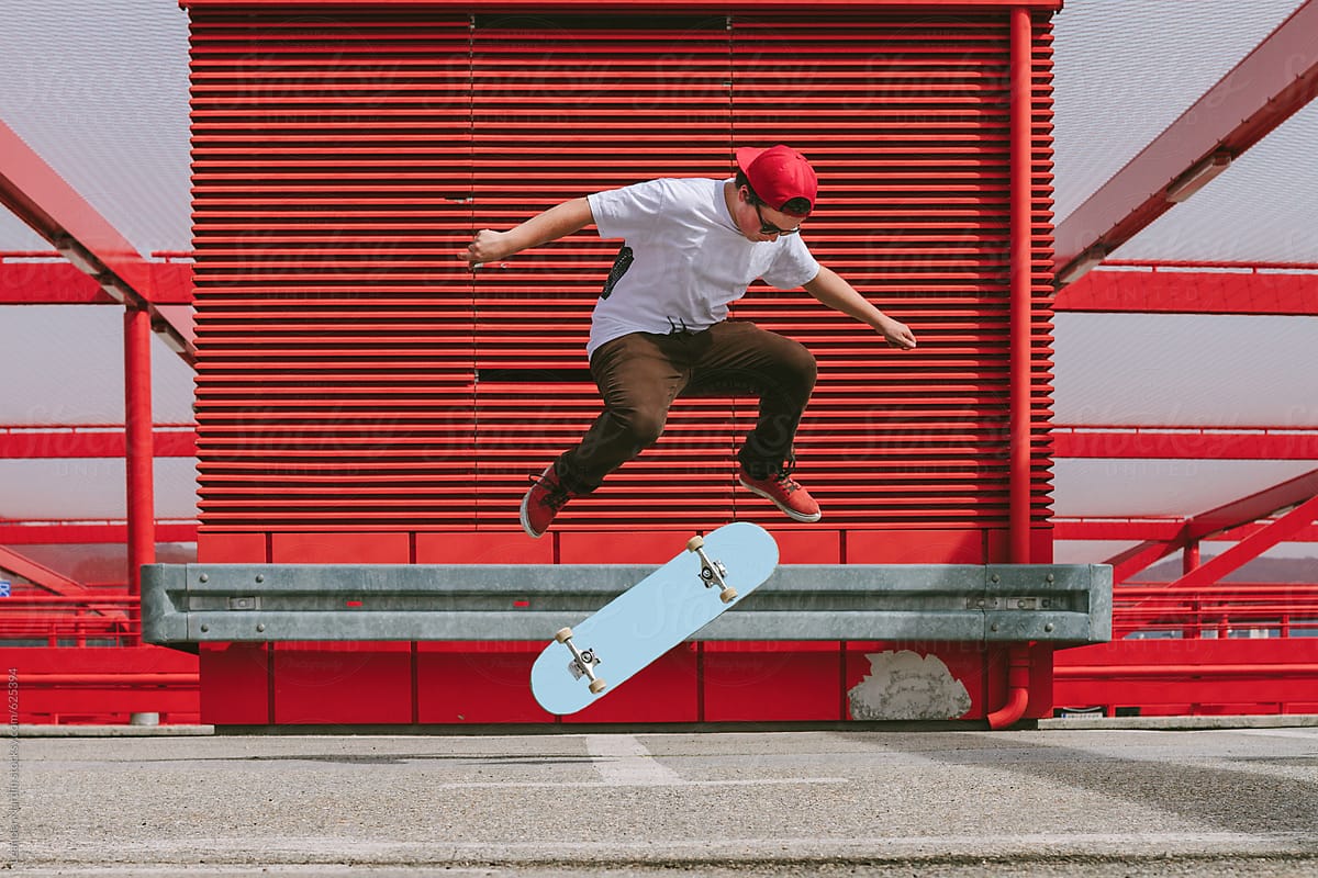 teenager doing a kickflip with his skateboard in red modern urban area