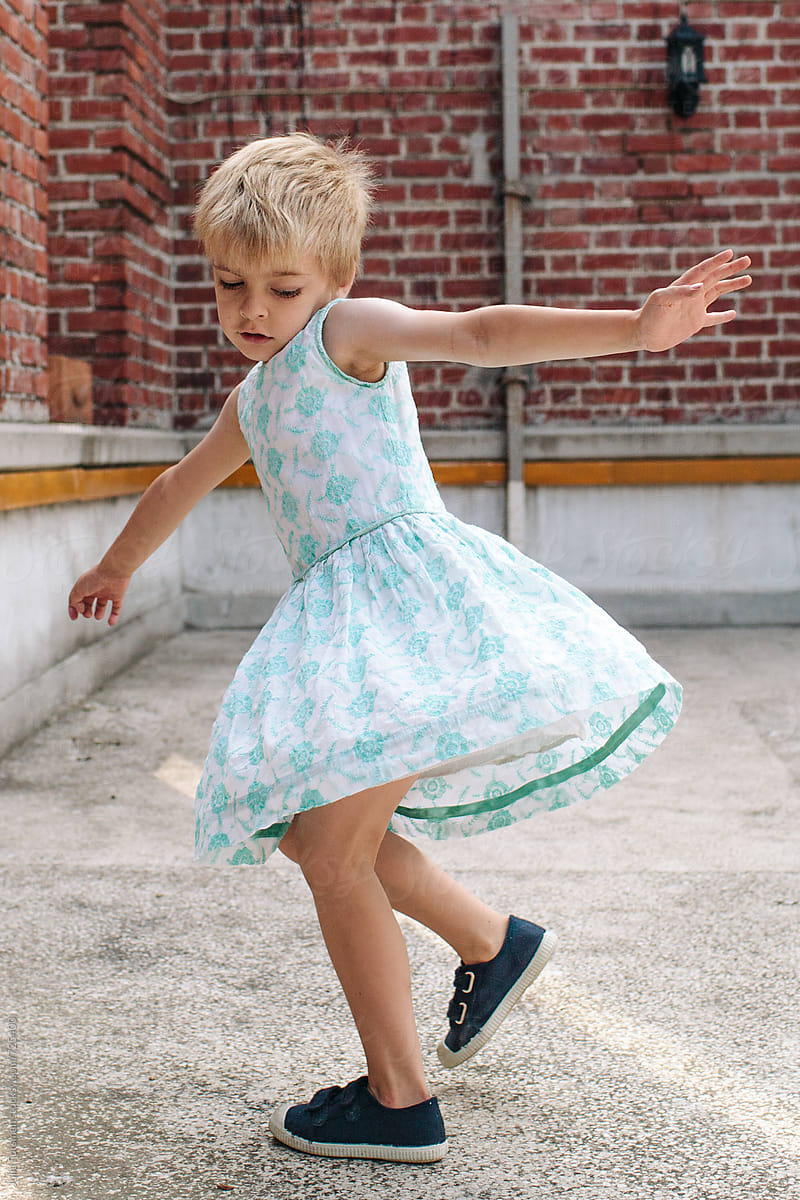 Blonde boy child spins around in a pretty dress.