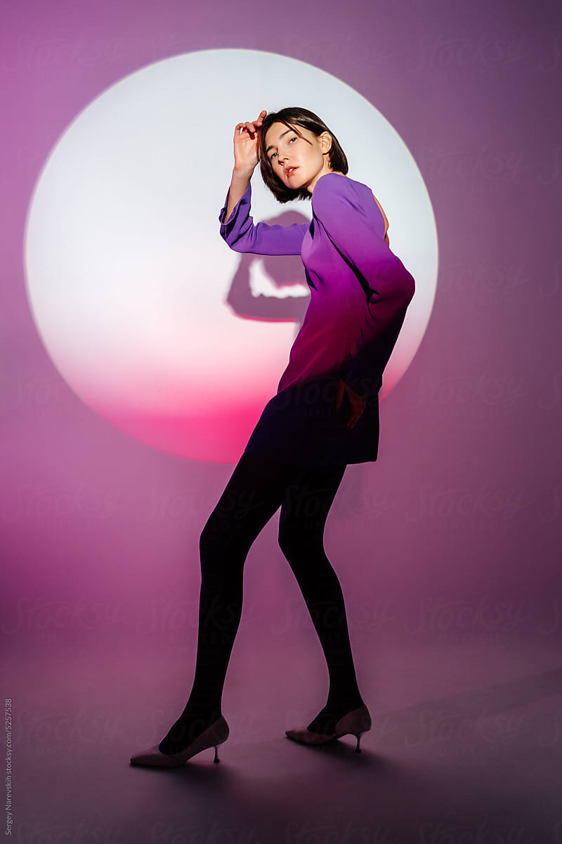 Female model in purple dress touching head while posing in studio