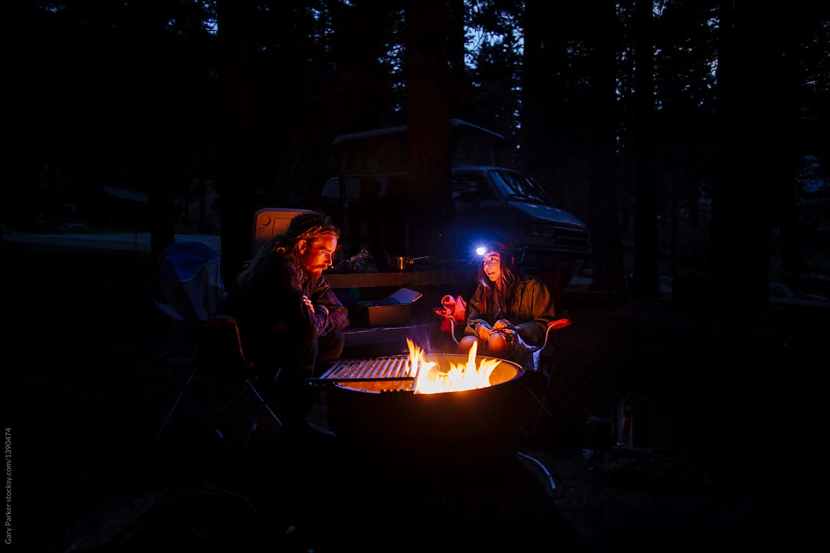 A couple sit close to a campfire at night