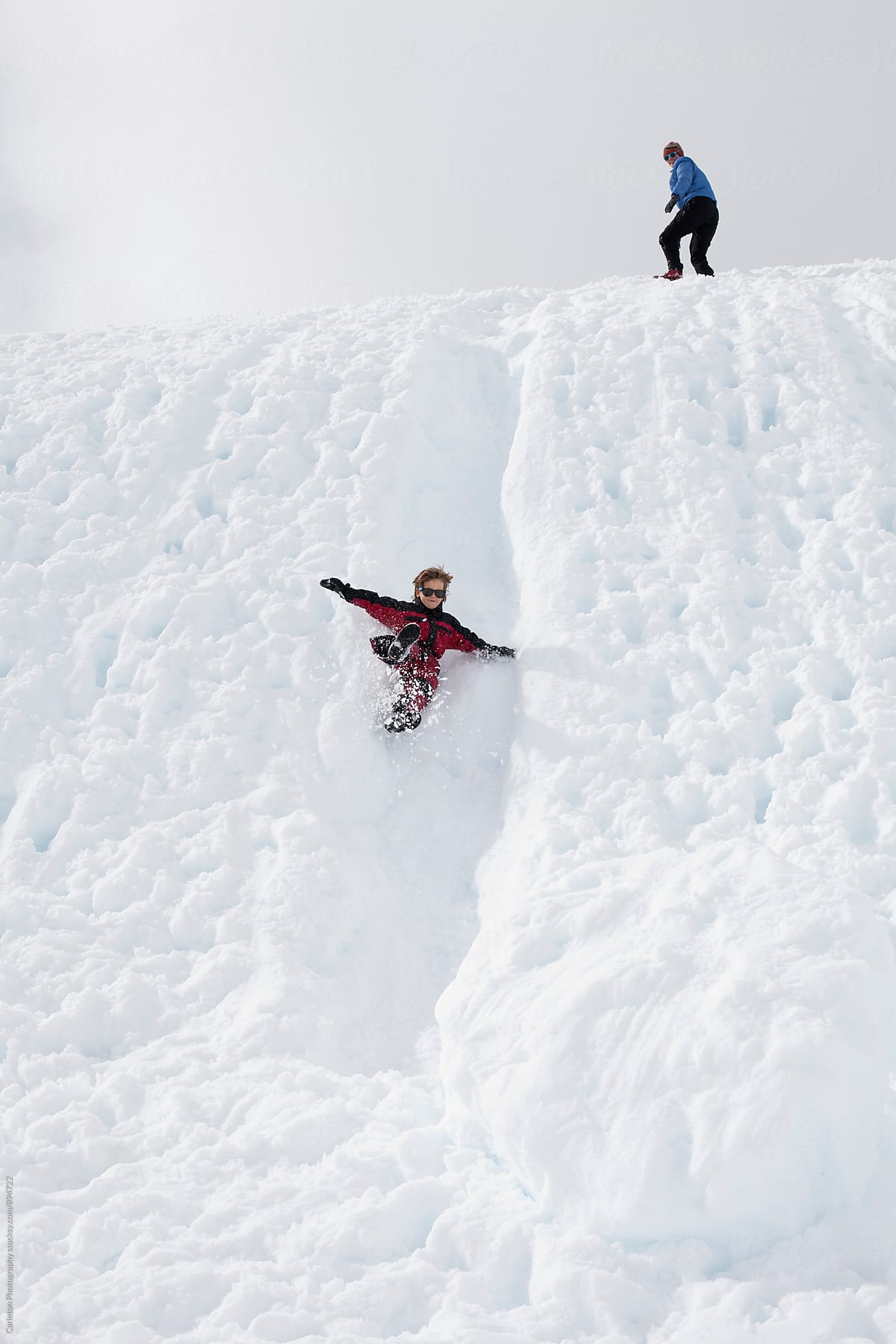Boy flies down a snowy chute while mom looks on from the top of the hill
