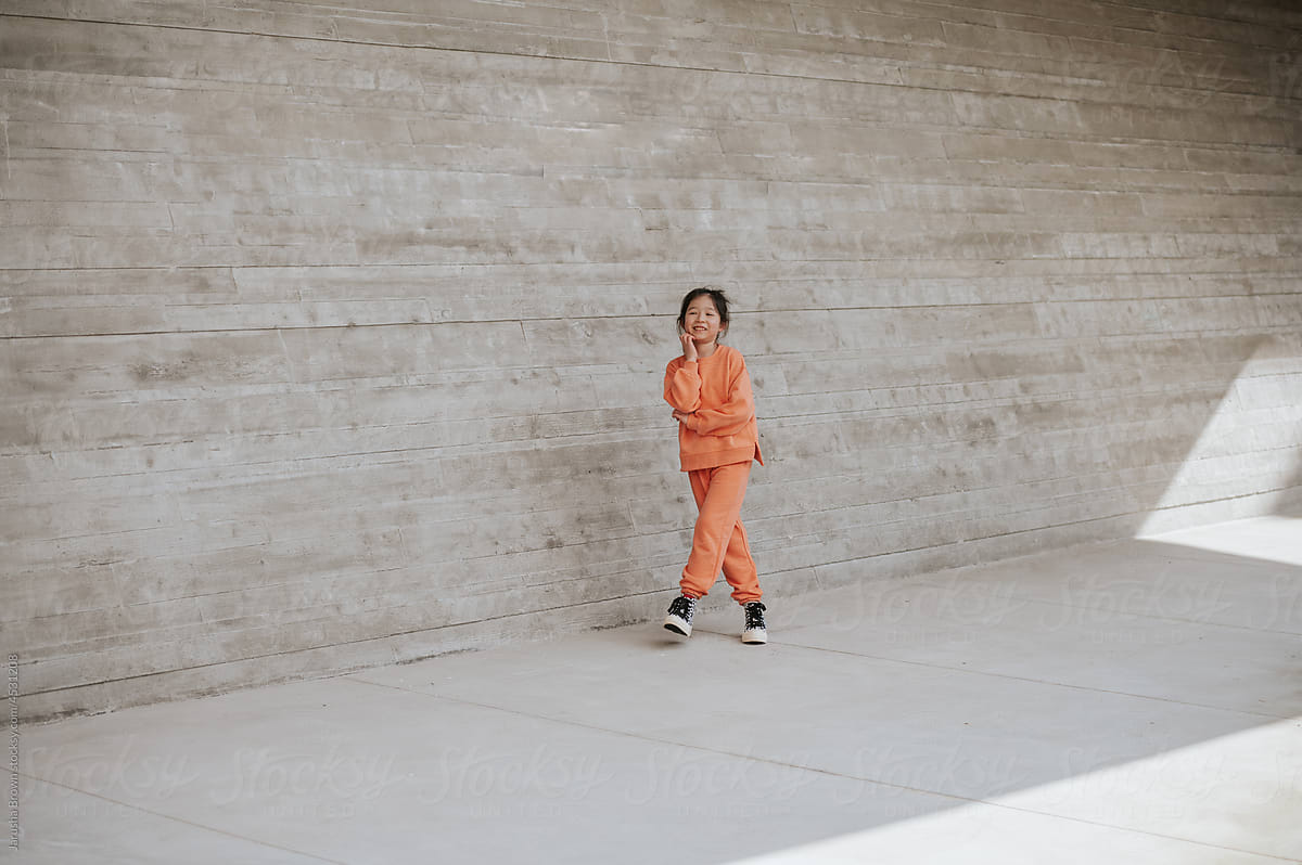 Young girl in workout clothes walks near a concrete wall.