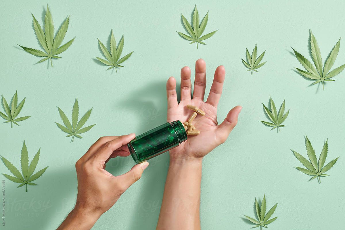 Herbal capsules in hand pour from green plastic pills jar.