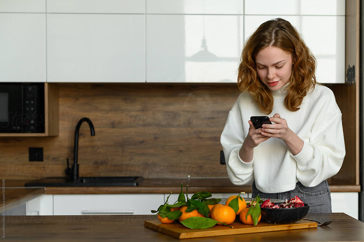 Woman using mobile phone before cooking at home