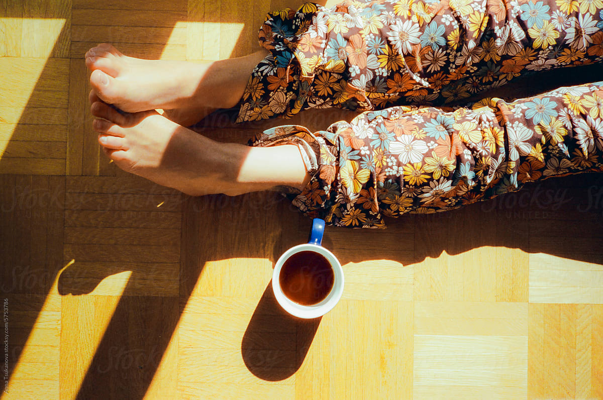 Woman laying on hardwood floor drinking coffee and enjoying sunshine