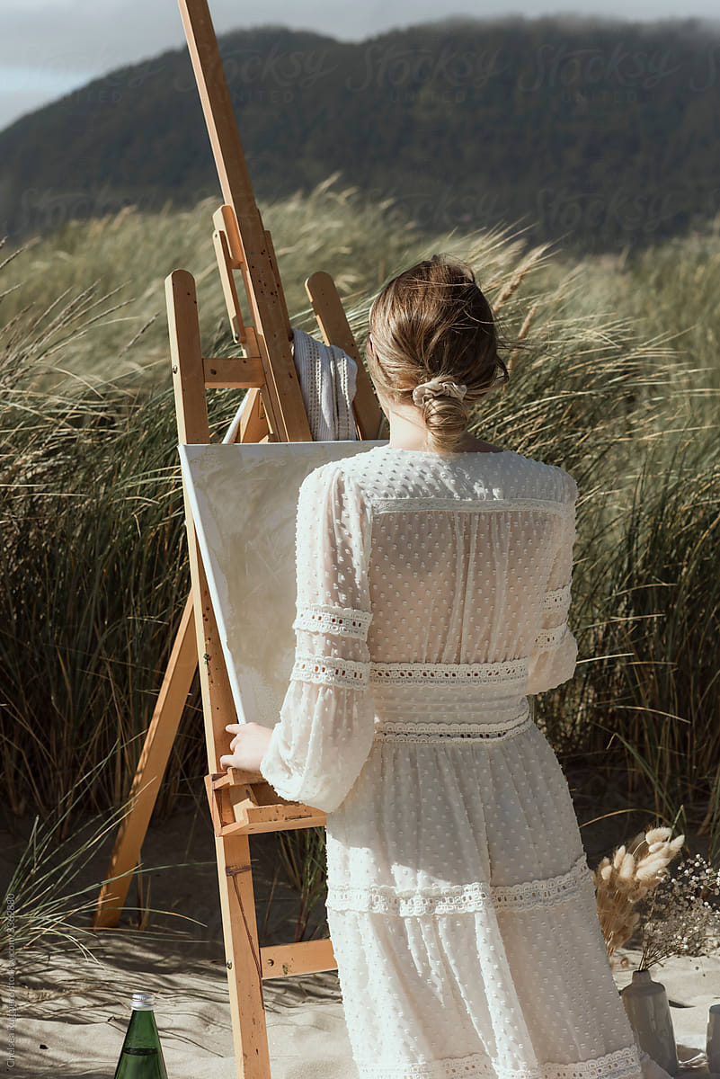 Stylish woman painting on an easel in the dunes