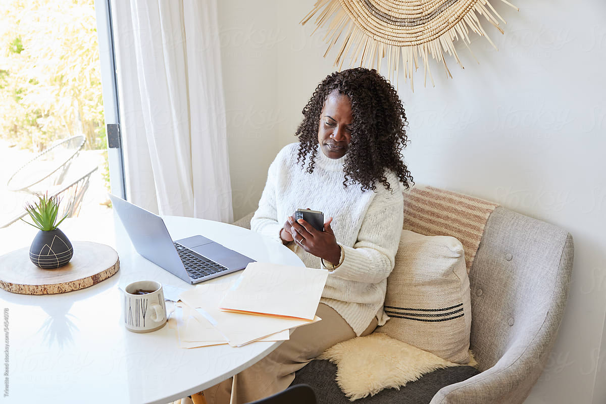 Mature Black woman paying bills online on computer and phone at home