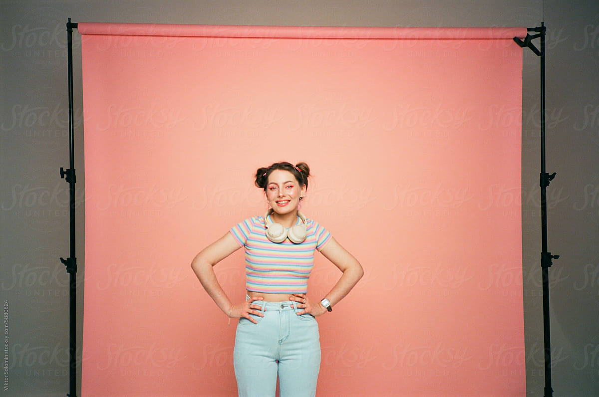 Cheerful young woman standing near peachy paper background