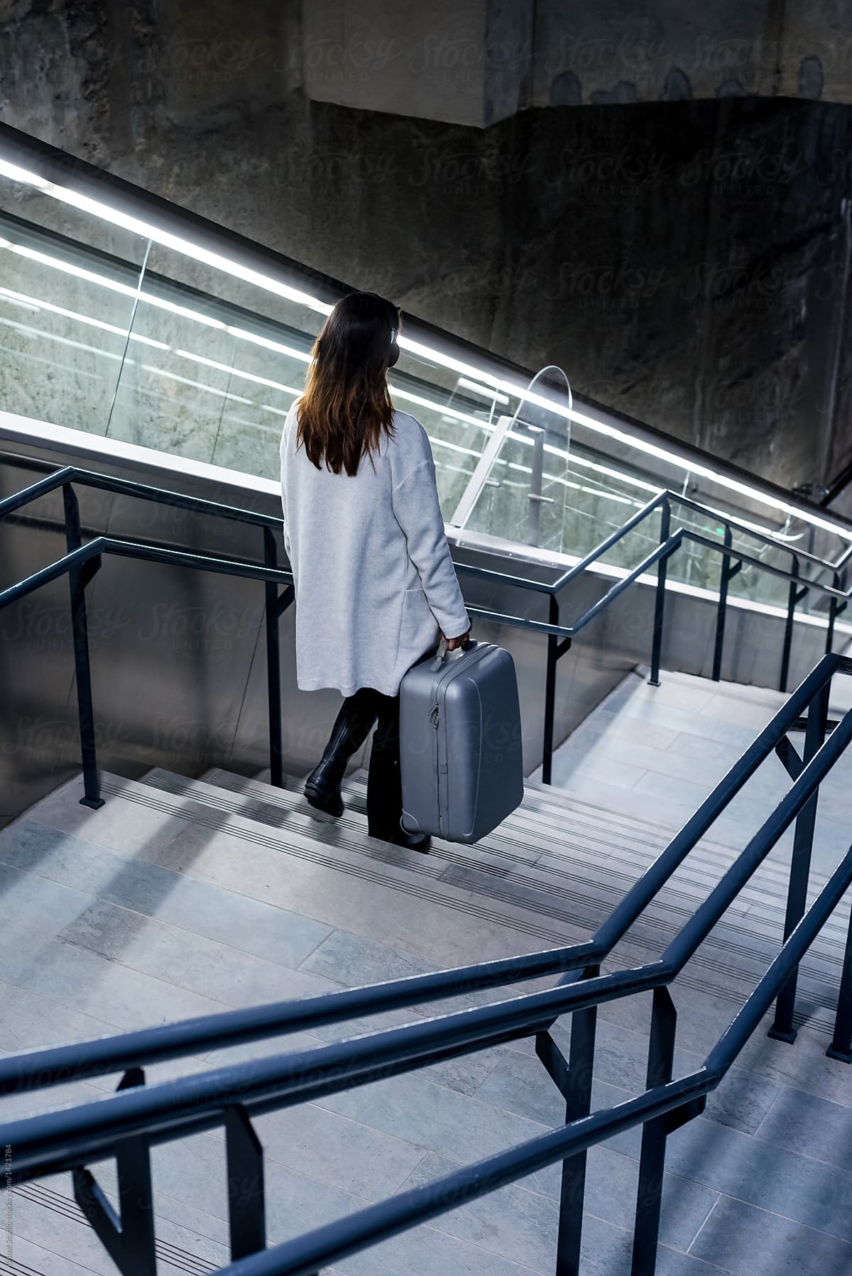 Female traveler in headphones on moving stairs