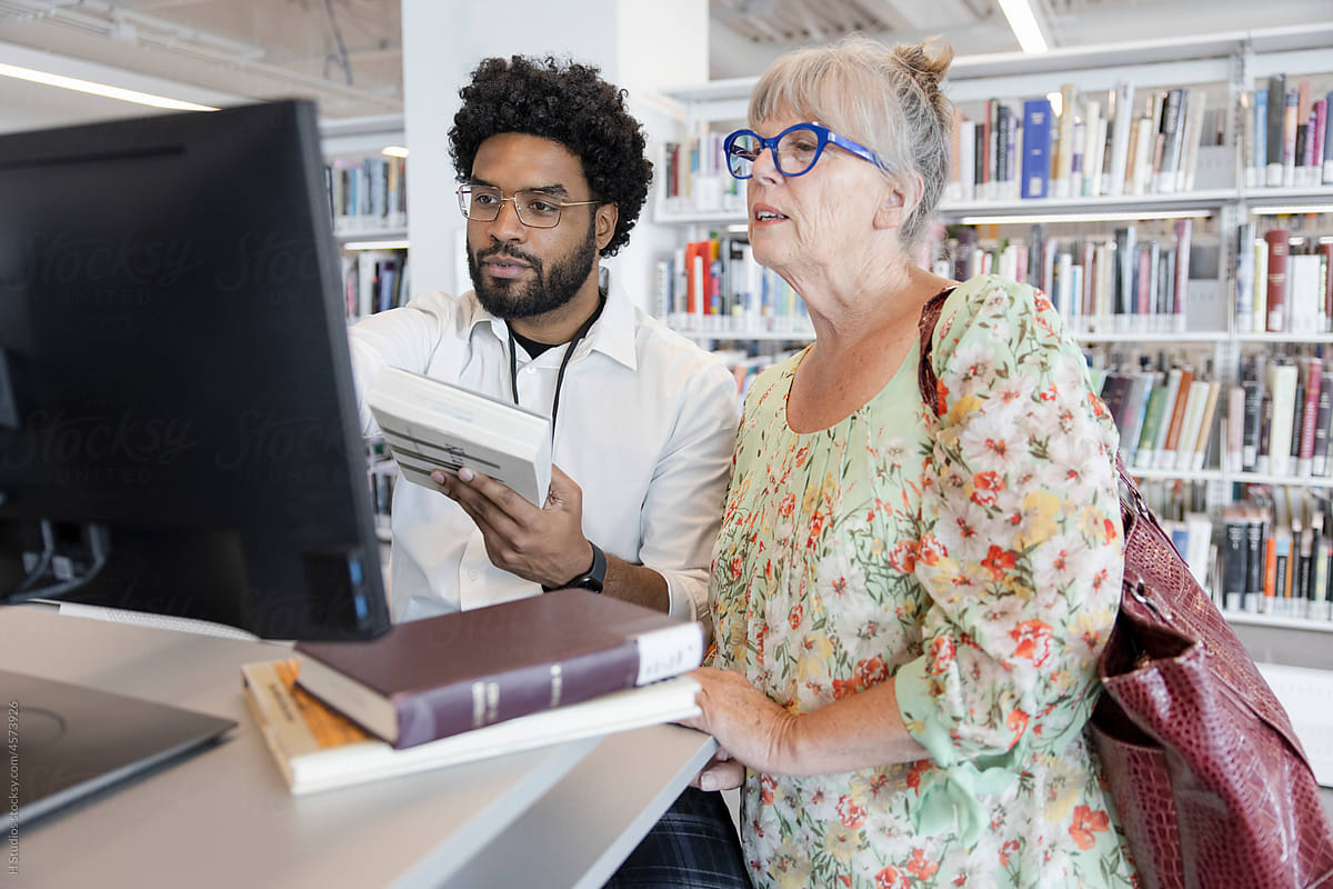 Male librarian helping senior woman check out books in library.