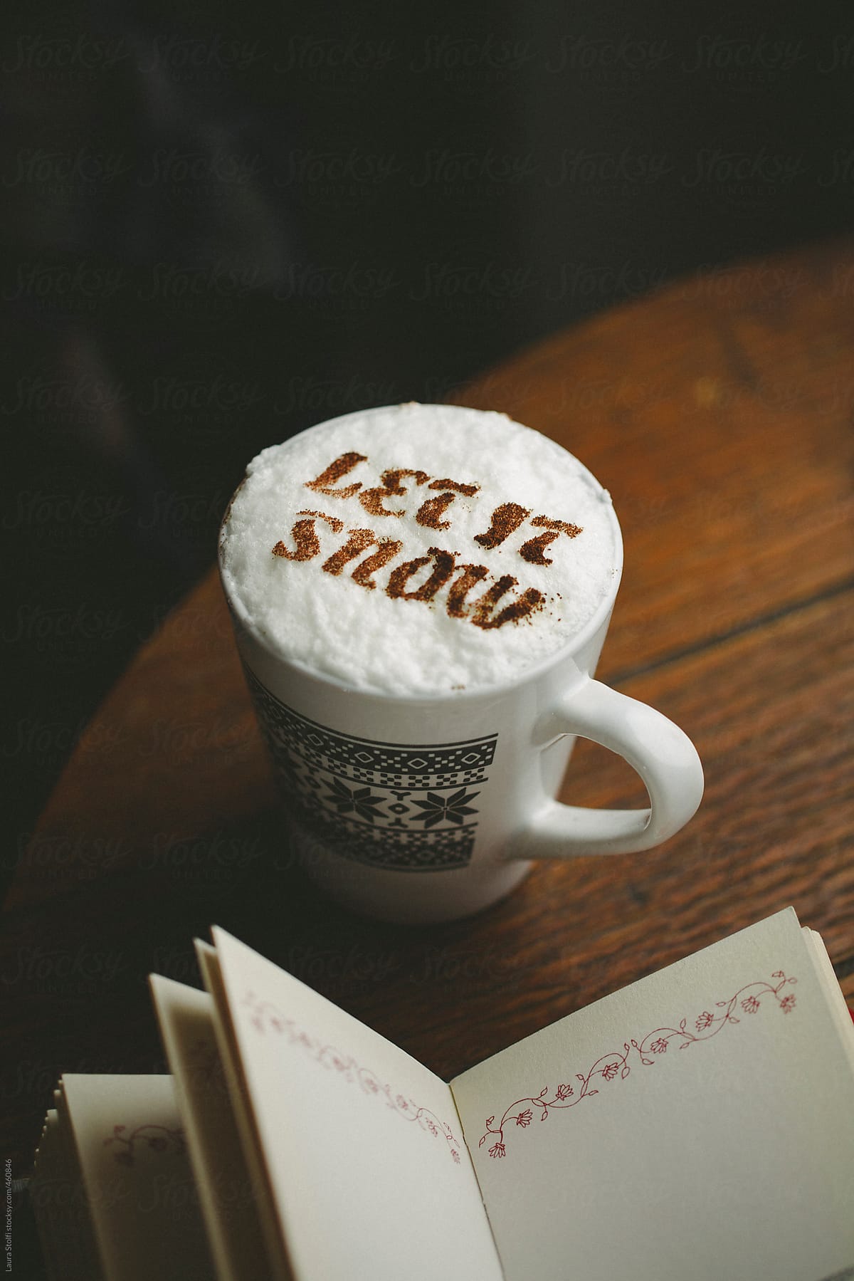 Hot chocolate mug with words Let it snow written with cacao powder on cream and book