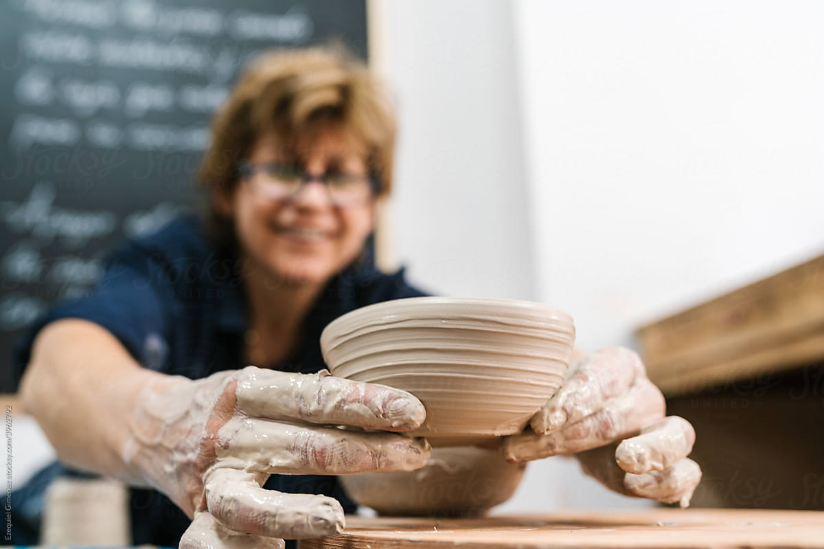 Smiling woman shaping wet clay pot
