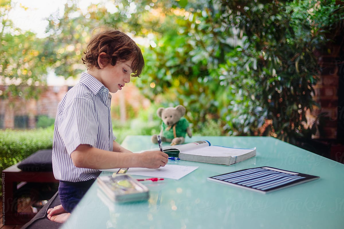 Boy sitting at an outside table doing his homework after school
