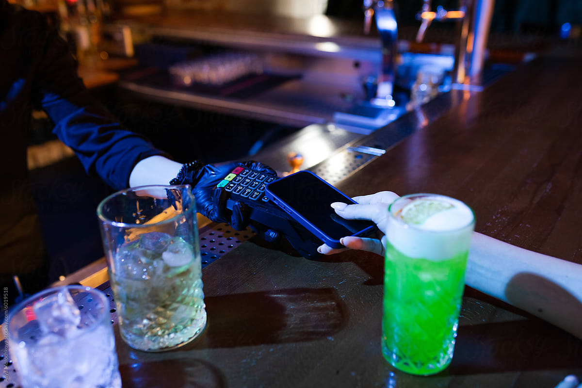 Woman paying for cocktails in the bar by mobile phone