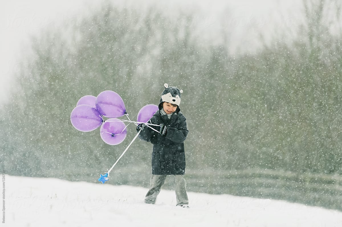 Child holding balloons in snow