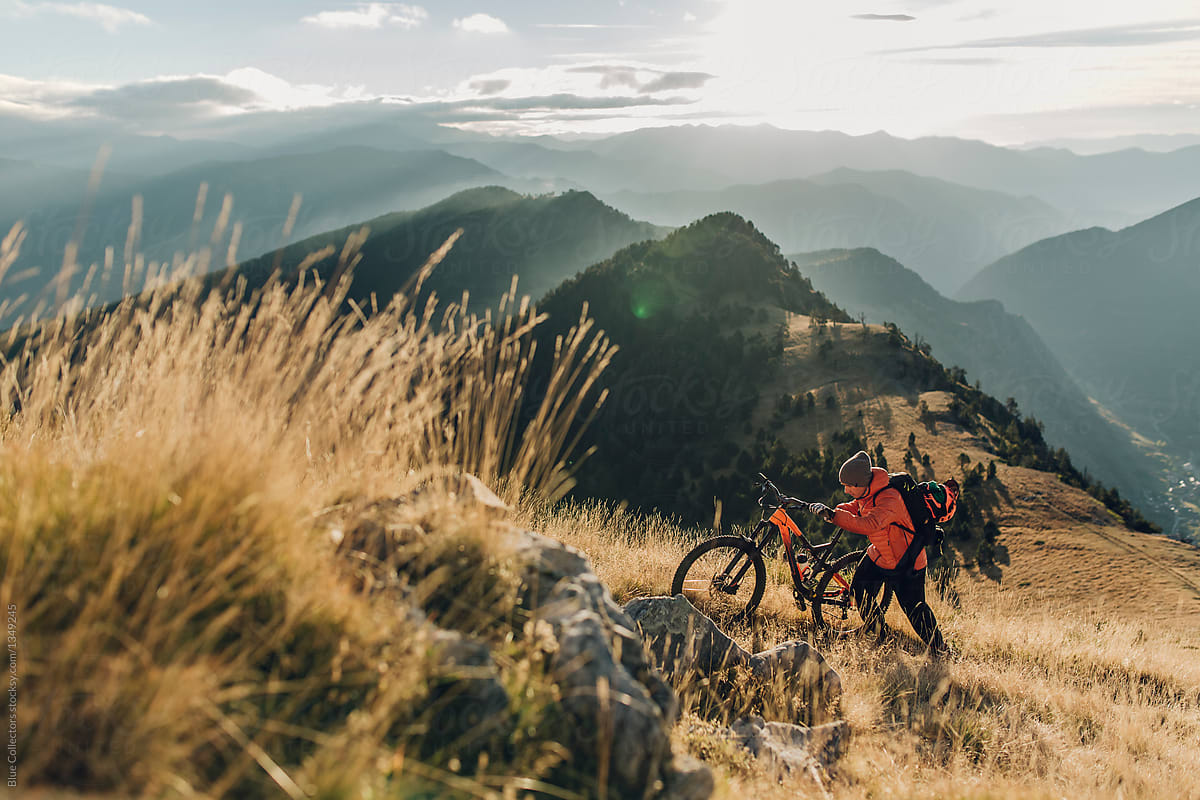 Young man carrying his mountain bike going up the mountain at the sunrise moment