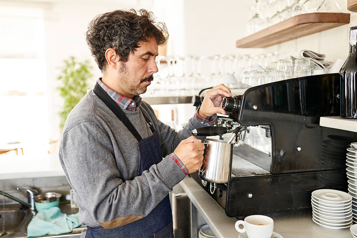 Waiter pouring hot milk from coffee maker in kitchen