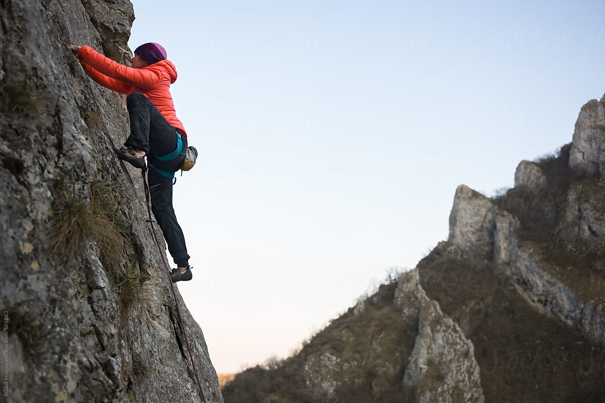 Woman climbing natural rocky wall with clear sky in the background