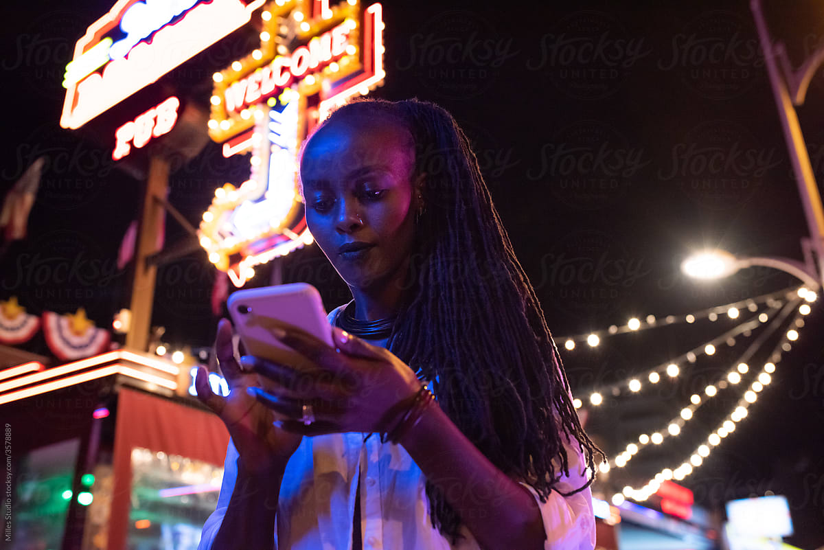 Black female browsing social media on street at night