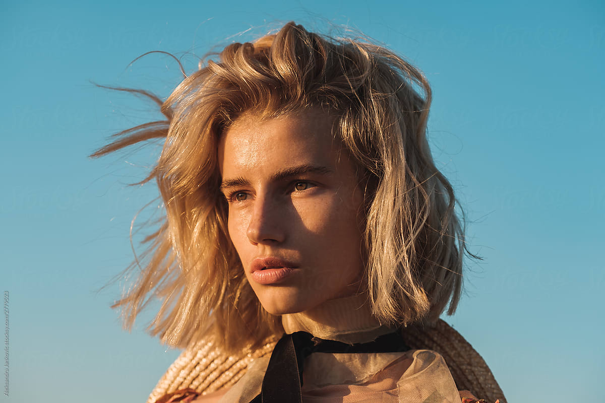 Close Up Portrait Of Fashionable Woman With Messy Blond Hair Against The Blue Sky