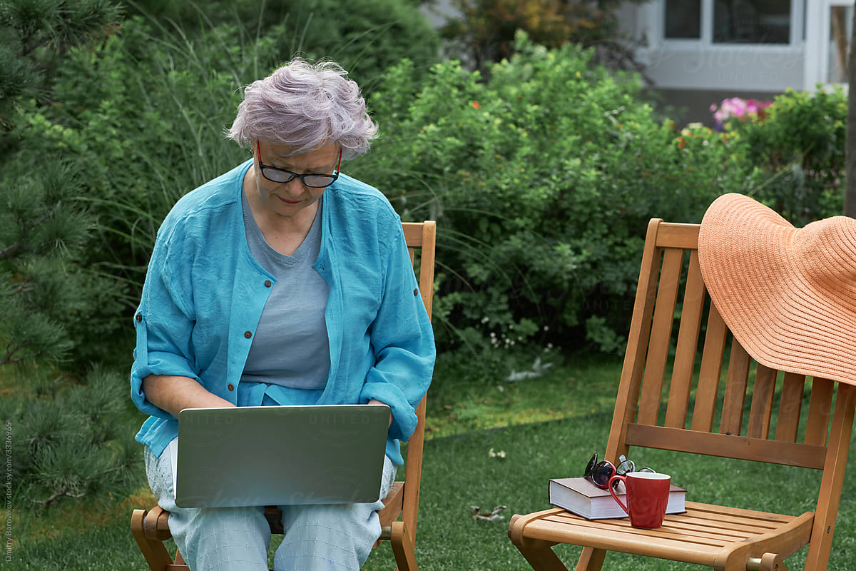 Beautiful elderly woman in her garden working at home on a laptop