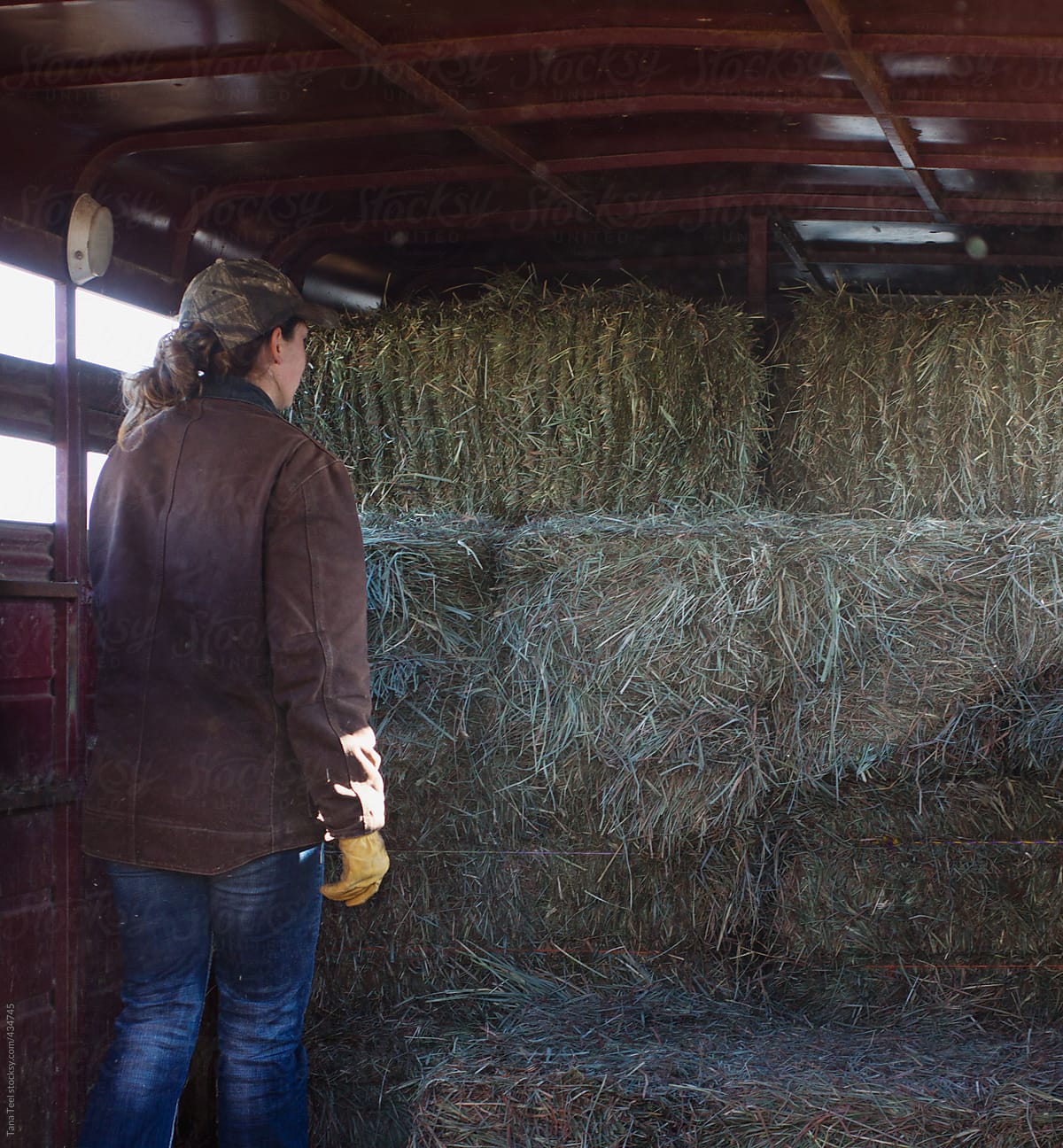 Farm girl standing by stacks of hay bales inside trailer