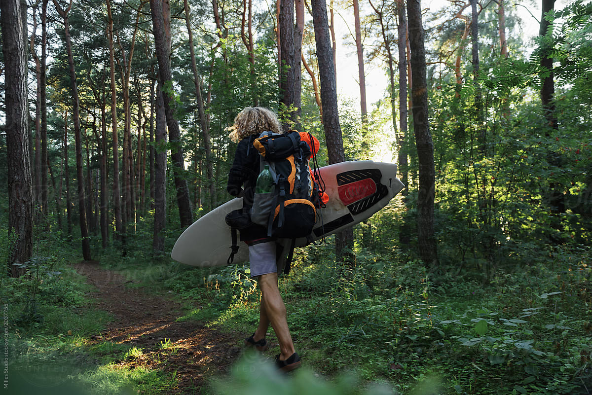 Traveler with backpack and surfboard in woods