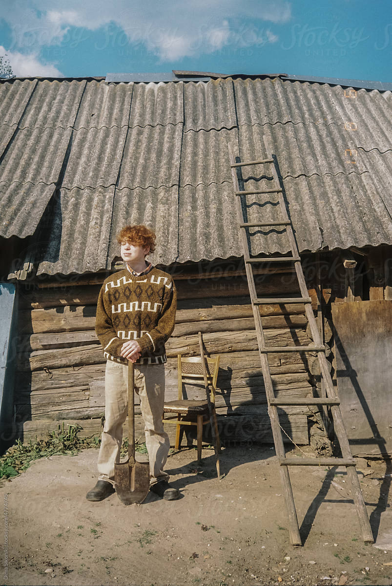 Attractive rustic red-haired guy stands with a shovel on the farm