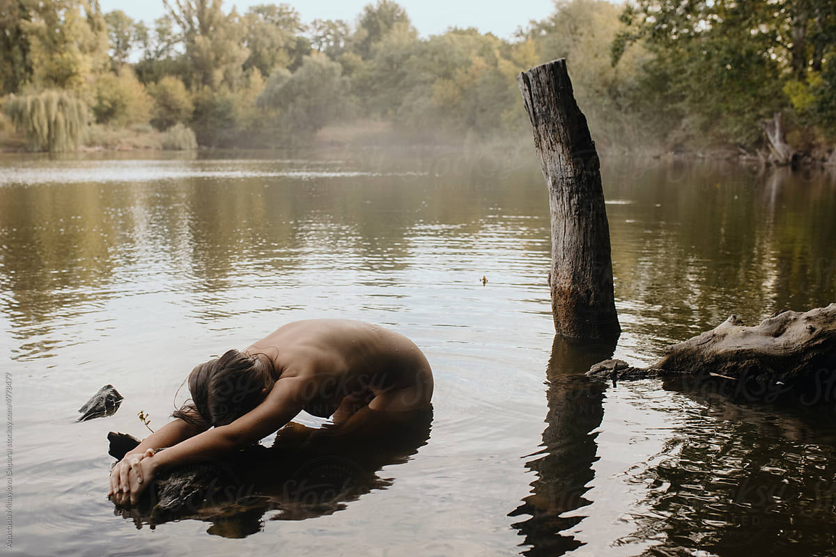 Nude tanned woman lying stretching on the bank of the river