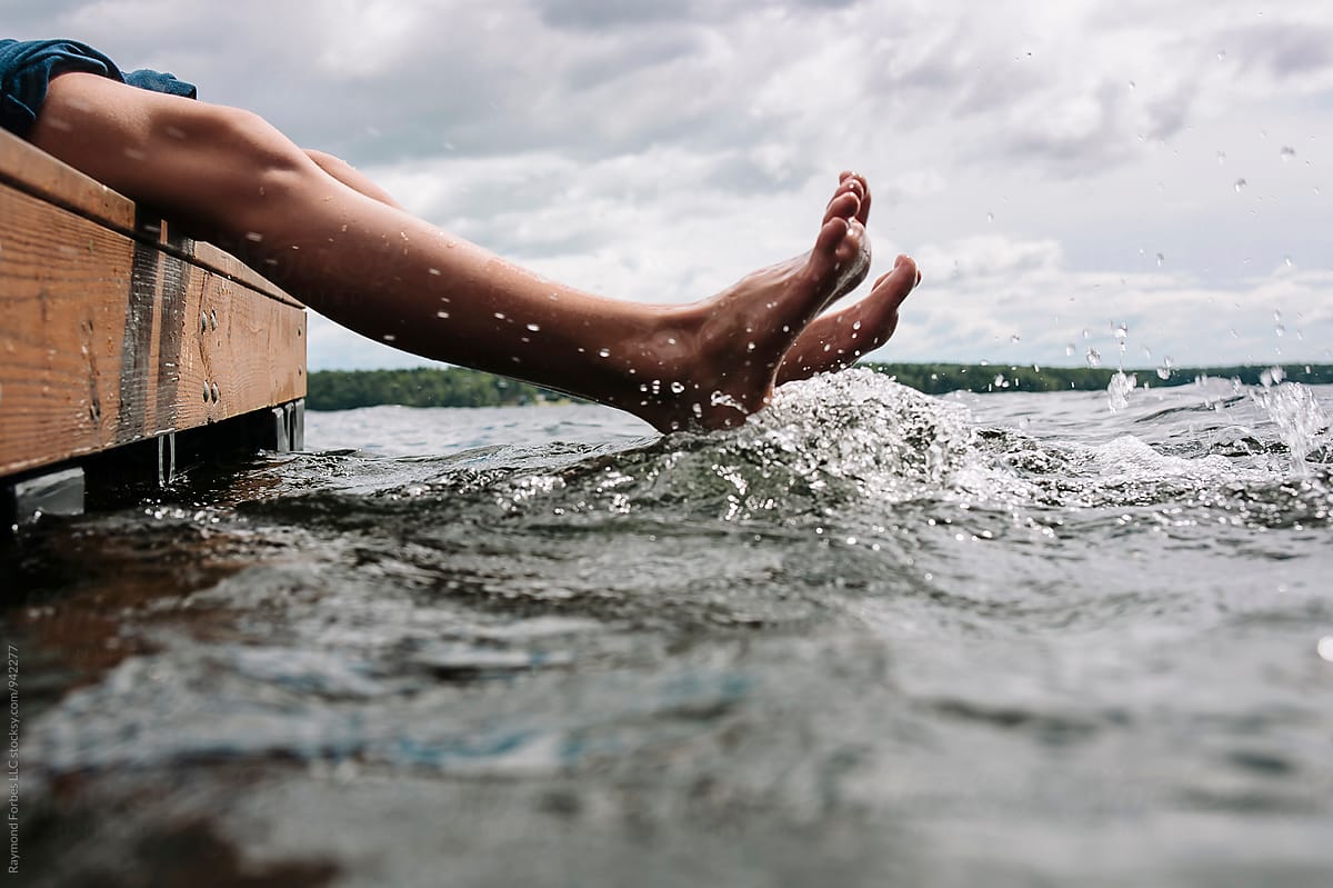 Feet splashing in water while sitting on dock